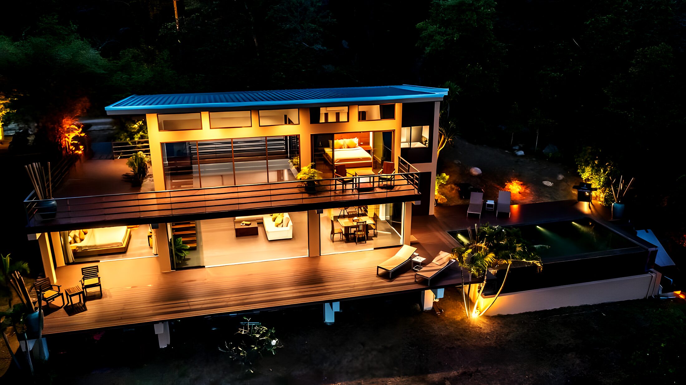 Aerial view of The Hideaway lit up at dusk, perched on the cliff above the sea