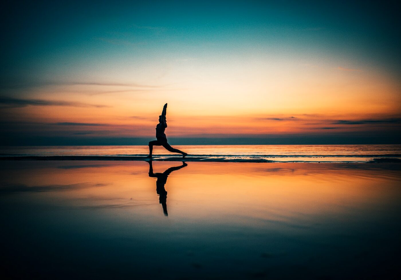 A silhouette practising yoga on a beach at sunset reflected in wet sand